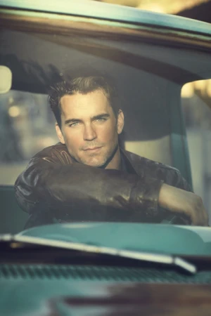 Portrait of a man in a leather jacket sitting inside a vintage car. The light emphasizes his face and the teal dashboard.