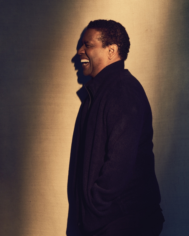 Smiling African-American man in dark jacket, side view, against warm-toned background, demonstrating joy and relaxed sophistication.