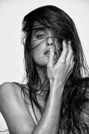 Close-up monochrome portrait of a woman with dark hair strands across her face and her hand raised near her lips.