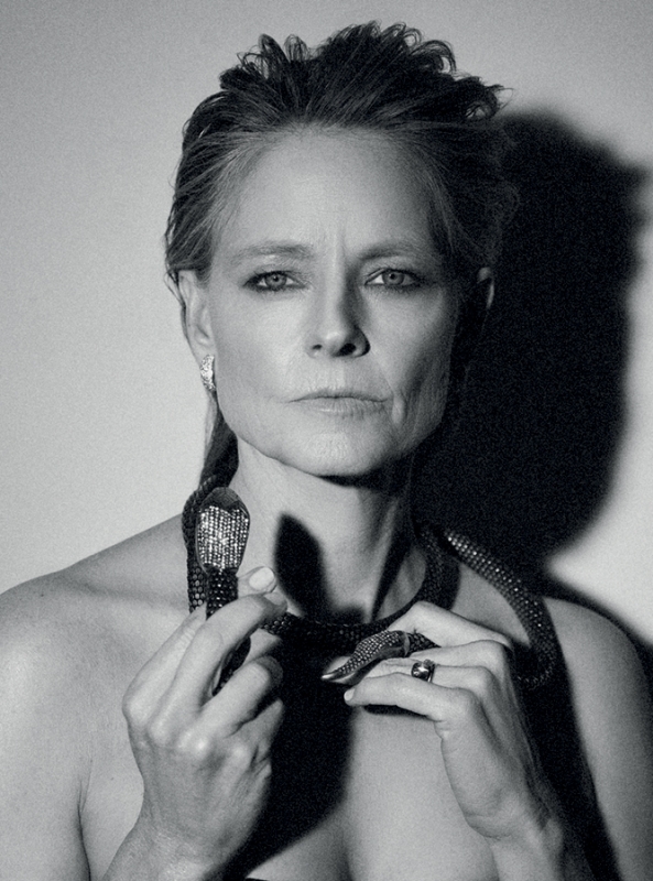 Black and white portrait of adult woman wearing a snake necklace and earrings, close-up shot against a neutral background.