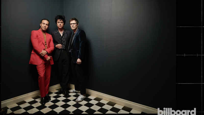 Three band members in formal wear pose indoors against a black wall on a black-and-white checkerboard floor in a portrait shot.