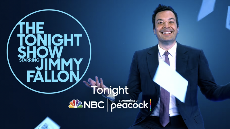 Jimmy Fallon in a suit smiles and throws cards in the air on The Tonight Show set with NBC and Peacock logos against blue background.