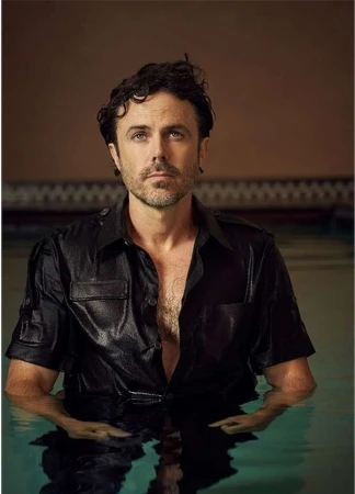 Portrait of a man in a wet, black, short-sleeved shirt, standing in water, with a blurred background, and focused on his upper body and face.
