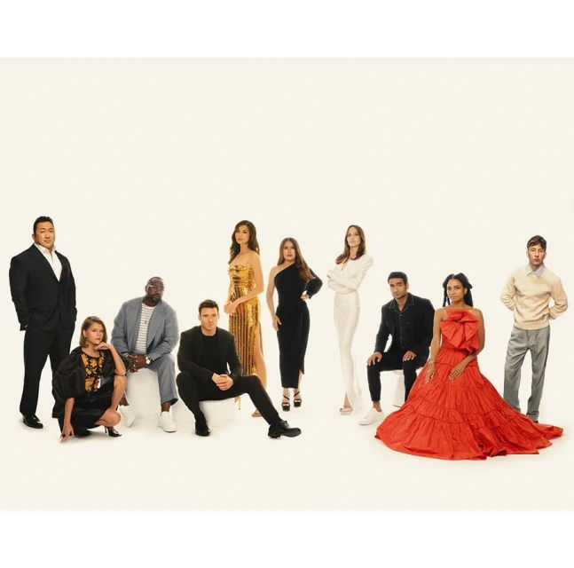 Group of eleven people in formal attire posing in a studio setting with a neutral background, showcasing a variety of elegant dresses and suits.