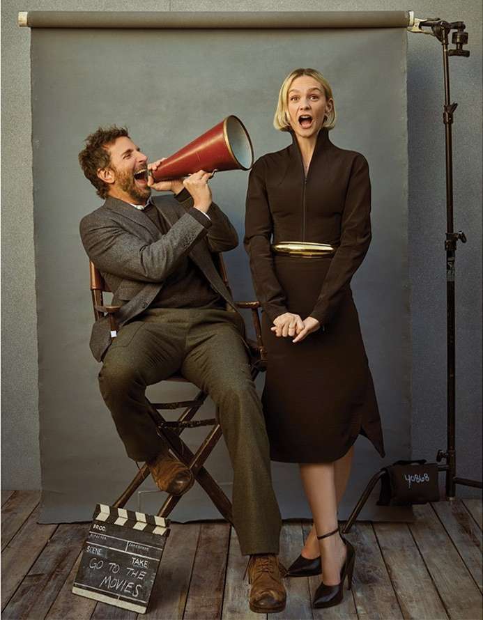 Man and woman pose with a megaphone and film slate in a photo studio, showcasing vintage fashion and cinematic style with a gray backdrop.