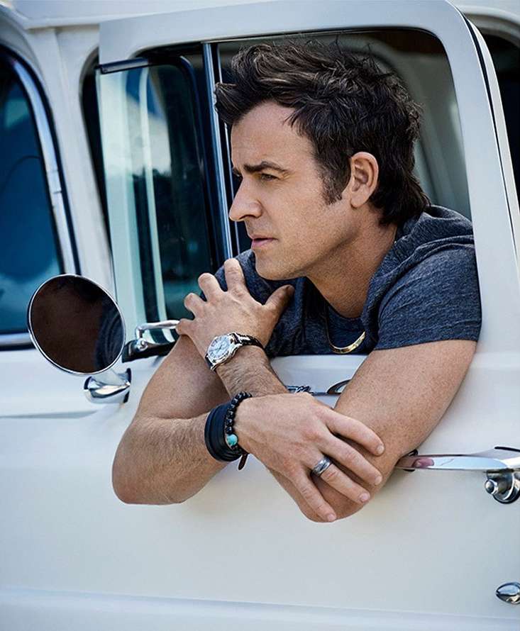 Portrait of a man leaning out the window of a white vintage truck, showcasing a watch, bracelets, and a ring on his hand.
