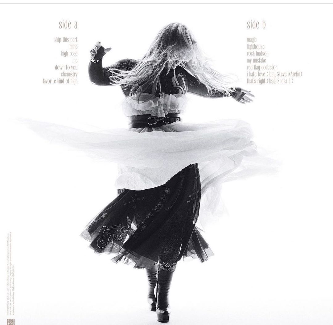 A woman wearing a black-and-white tulle dress with long blonde hair dances with her arms outspread on a white background in a studio shot.