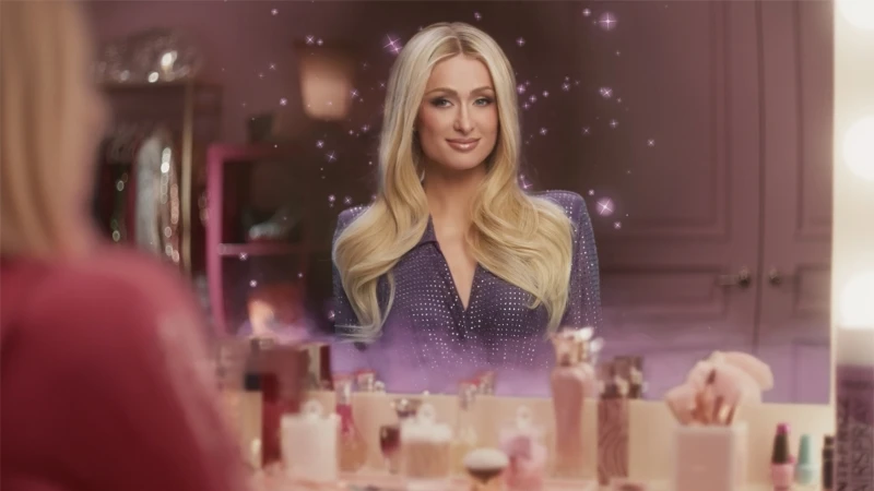 Close-up of a woman with long blonde hair in a purple shirt, reflecting in a vanity mirror surrounded by perfume bottles.