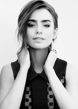 Monochrome portrait of Lily Collins holding her hands to her neck, wearing a dark patterned dress against a plain light background