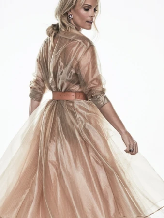 Blonde woman wearing a translucent organza dress with a wide belt against a white background
