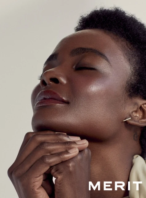 Close-up beauty shot of a smiling African American woman with her eyes closed and her hands folded, with the Merit brand name visible.