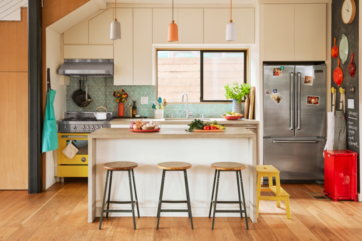 Bright, modern kitchen with wooden floors, white cabinets, island with bar stools, and stainless steel appliances under pendant lights.