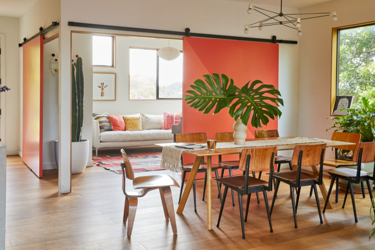 Open-concept dining room with wooden chairs around a table, monstera leaf centerpiece, and a sliding barn door with colorful panels.