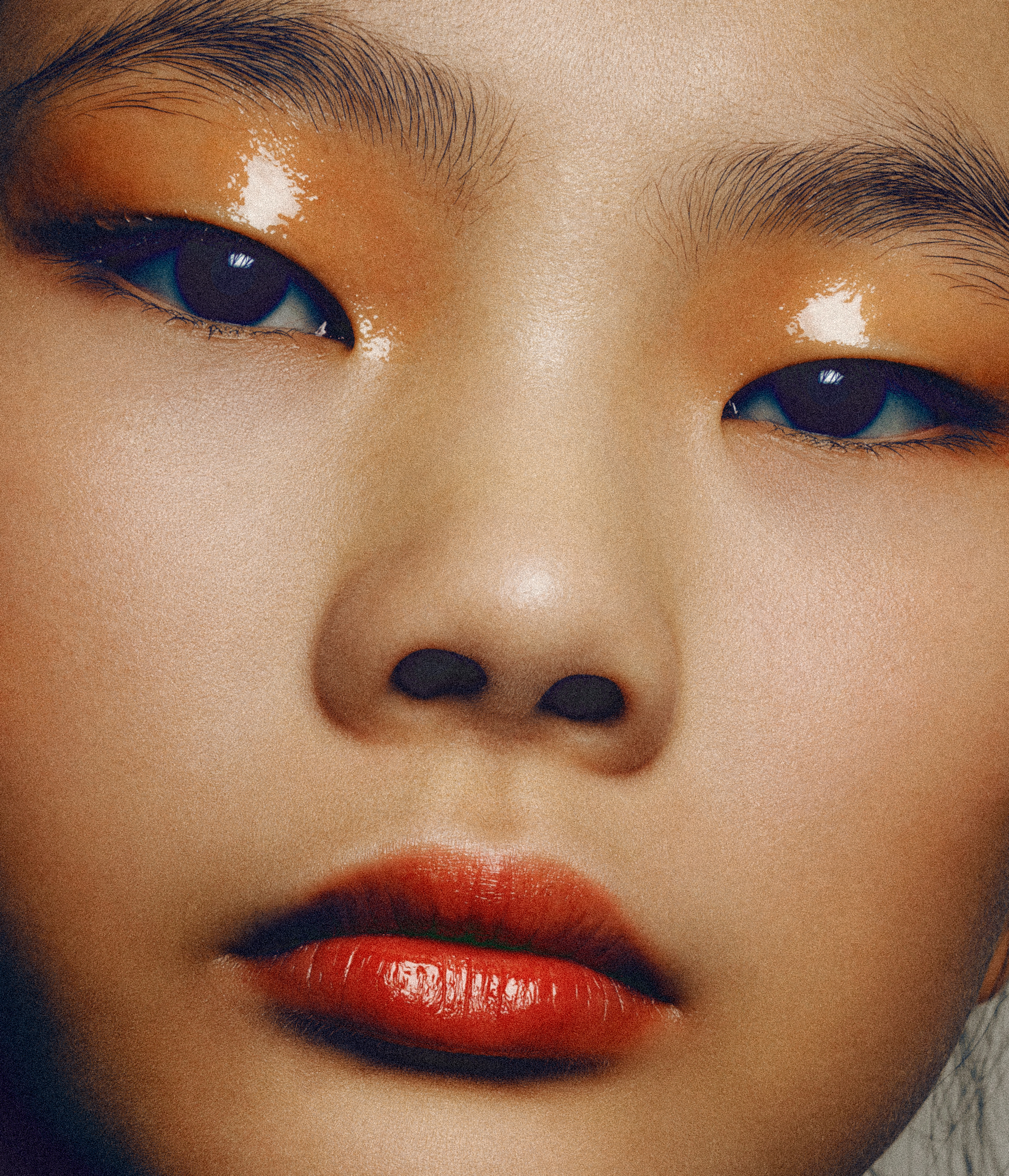 Close-up portrait of a young Asian woman with glossy orange eyeshadow and bright red lipstick, showcasing makeup and beauty.