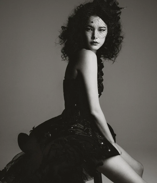 Portrait of an adult female model wearing a black dress with a veil, posing in a studio with neutral background and soft lighting.
