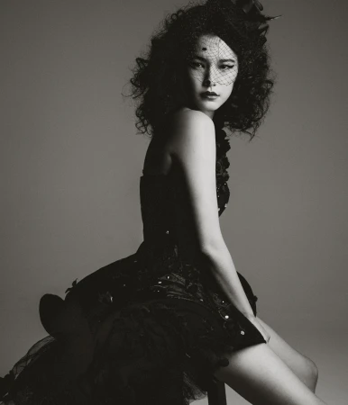 Portrait of an adult female model wearing a black dress with a veil, posing in a studio with neutral background and soft lighting.
