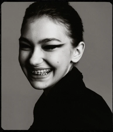 Black and white portrait of a smiling young woman with braces, wearing a black turtleneck sweater against a plain grey backdrop.