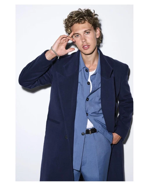 Portrait of adult male model in a blue suit and matching overcoat posing in a photo studio against a white seamless backdrop.