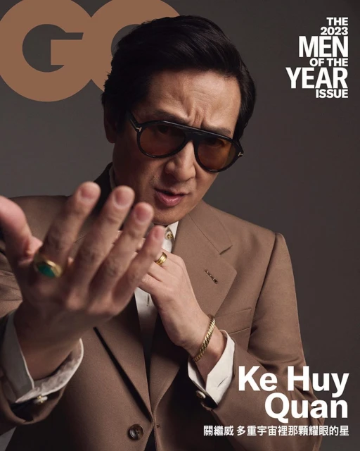 GQ magazine cover featuring Ke Huy Quan in a brown suit and sunglasses, holding out his hand towards the camera on a neutral gray background.