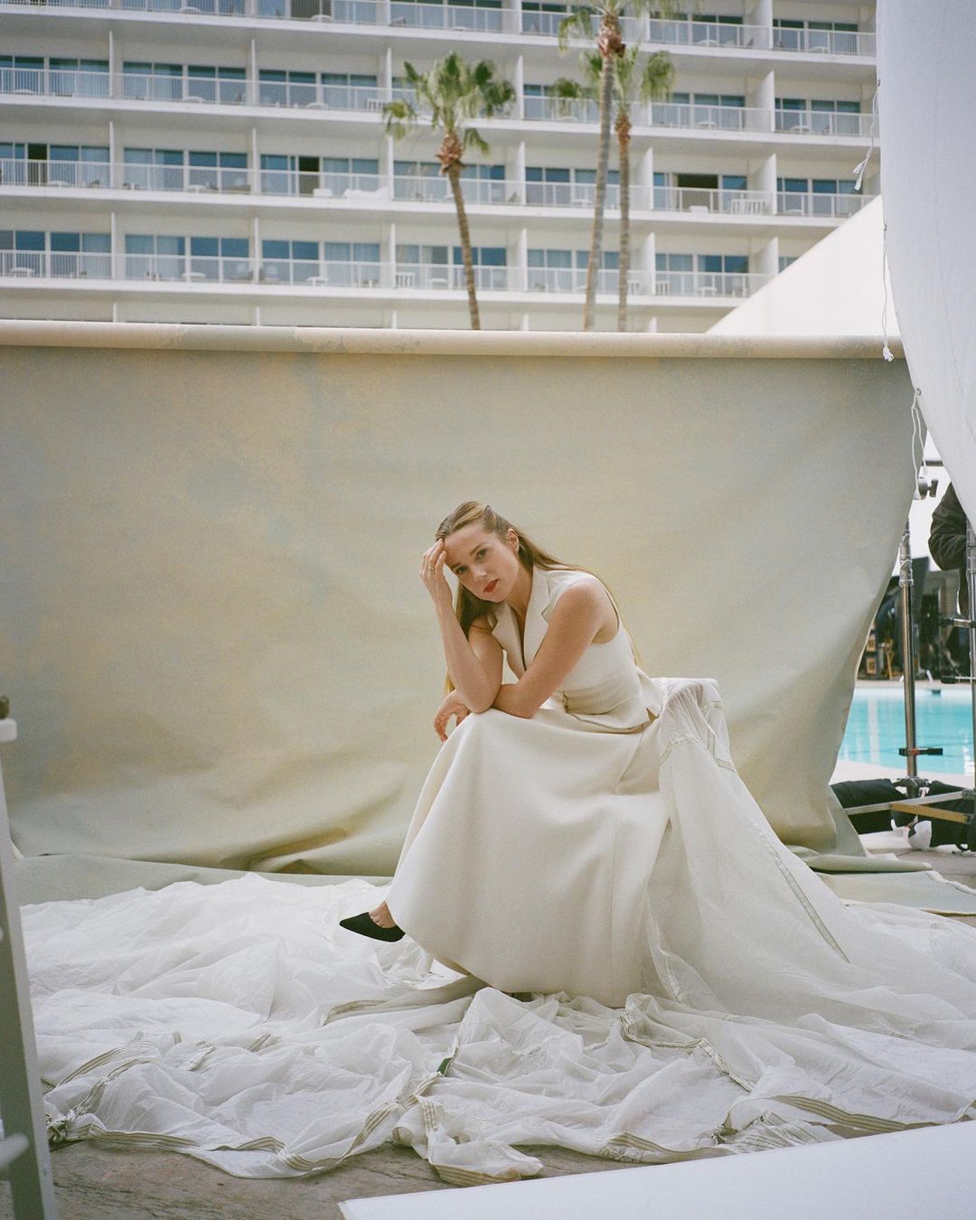 Woman in dress poses on set with modern architecture and palm trees in the background, creating a visually striking fashion image.
