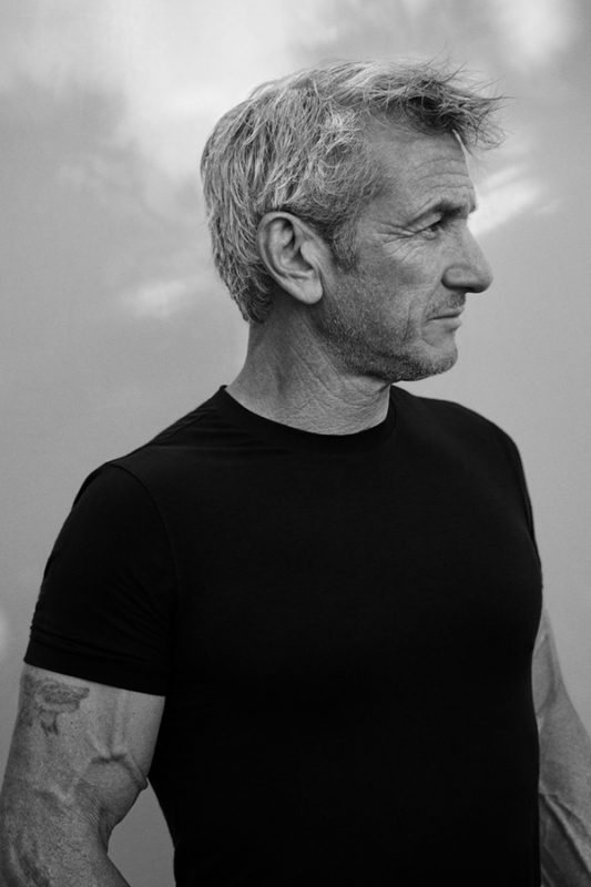 Portrait of a mature adult man in a black t-shirt, facing to the right, with gray hair against a neutral outdoor background.