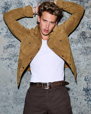 Attractive male fashion model in a suede jacket poses against a textured backdrop in a studio setting, showcasing his style.