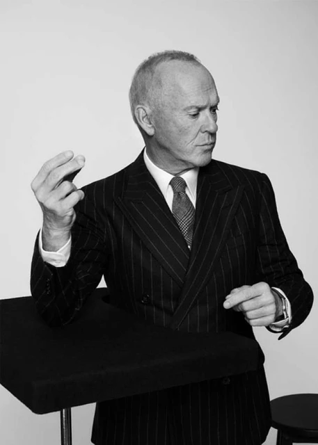Black and white portrait of a mature adult man in a striped suit looking to the right, hands gesturing, posing in a photo studio.