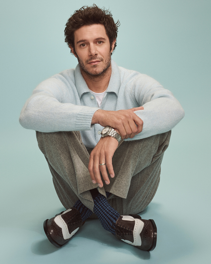 Man with light blue sweater and grey trousers seated against a light teal studio backdrop by Eric Ray Davidson