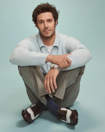Man with light blue sweater and grey trousers seated against a light teal studio backdrop by Eric Ray Davidson