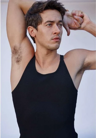 Portrait of a man in a black tank top with arms raised, photographed by Eric Ray Davidson against a plain background.