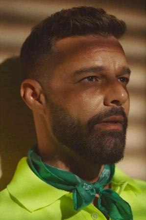 Close-up of a man with short brown hair and a beard, wearing a green scarf and a neon yellow collared shirt against a neutral background.