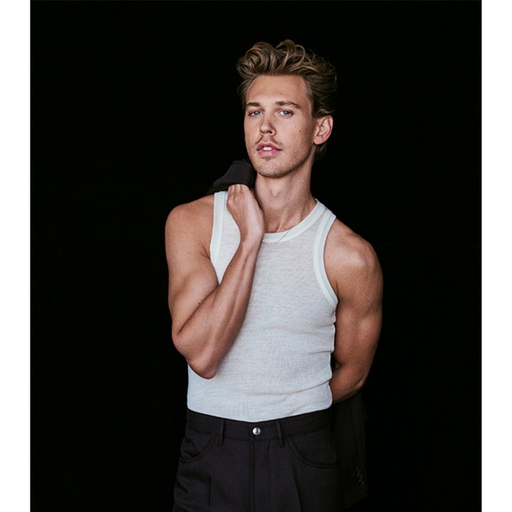 Actor Austin Butler wearing a white tank top and dark trousers against a black background in a portrait by Eric Ray Davidson.