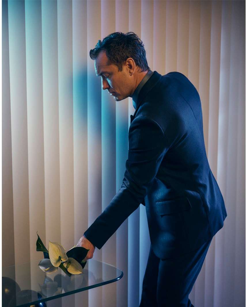 Portrait of a handsome man in a suit tending to flowers on a table, captured in a photo studio with dramatic lighting.