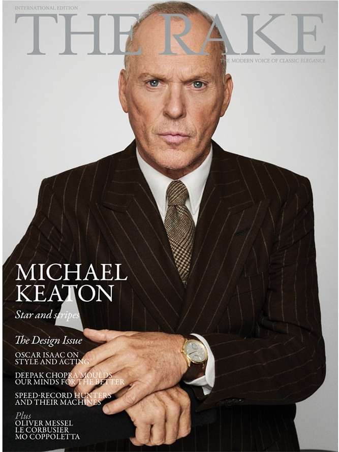 Michael Keaton on magazine cover, wearing pinstripe suit with hands folded; close-up shot featuring watch, tie, and neutral studio backdrop.