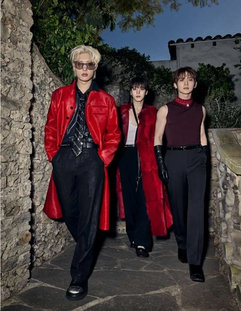 Three stylish Asian men walk on a stone path outdoors. They are wearing fashionable clothing including red jackets and shiny black pants.