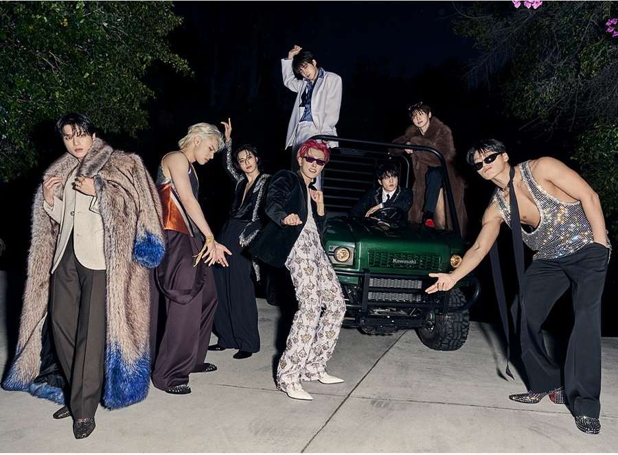 Group of stylishly dressed young adults posing next to a green Kawasaki vehicle at night. Fashion and entertainment editorial.