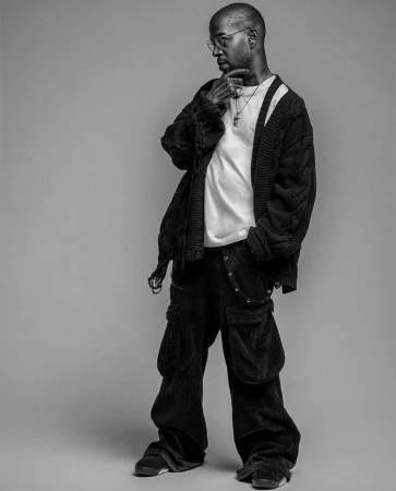 Monochromatic portrait of a stylish adult male in a casual white t-shirt, oversized cardigan, baggy pants, jewelry, and glasses looking left.
