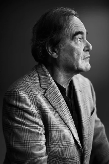 Black and white portrait of an adult man with dark hair wearing a plaid blazer, looking right with a neutral facial expression.