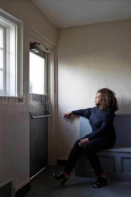 Portrait of Jamie Lee Curtis in a black turtleneck and blazer in front of a grey backdrop with soft, diffused lighting.