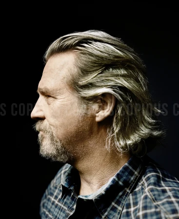 Profile portrait of Jeff Bridges with long grey hair and a beard, wearing a dark plaid shirt against a dark background.