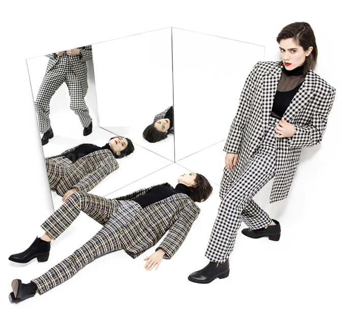 Fashion editorial shot of a female model wearing a black and white checkered suit, posing in a photo studio with mirrors.
