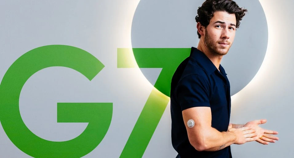 Adult man stands with arm monitor on a light grey background with green G7 text and halo light, promoting wellness and healthcare.