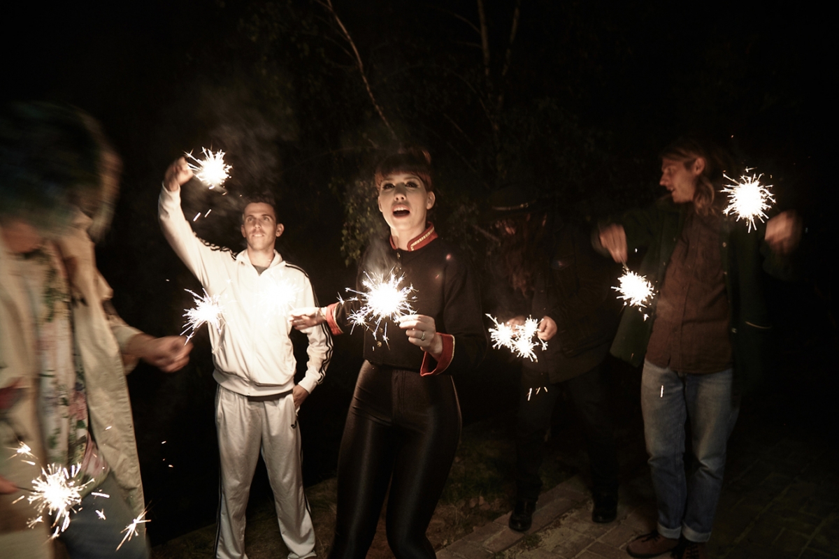 Group of friends celebrating at night with sparklers. Dark outdoor setting with people holding sparklers, creating a festive atmosphere.