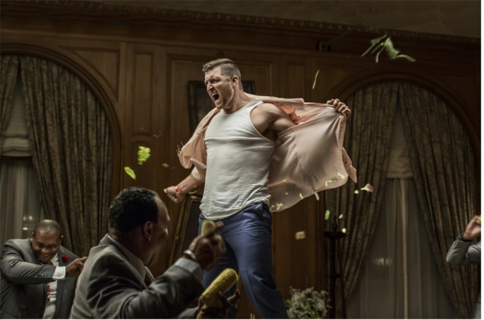 Man in tank top and dress shirt, angry expression, throwing corn cobs surrounded by men in suits in an ornate dining room setting.