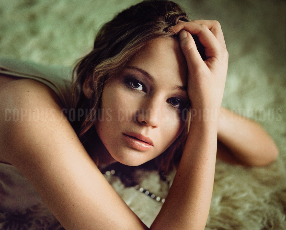 Portrait of Jennifer Lawrence resting her head on her hand against a textured soft background, photographed by Pamela Littky.