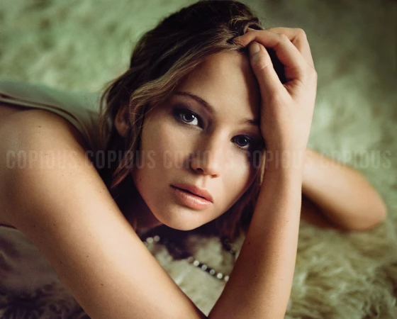 Portrait of Jennifer Lawrence resting her head on her hand against a textured soft background, photographed by Pamela Littky.