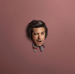 Man winking and shouting through a hole in a mauve wall, wearing a patterned bow tie.