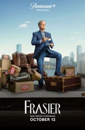 Kelsey Grammer posing on a stack of luggage with a coffee cup in a blue suit outdoors by a city skyline