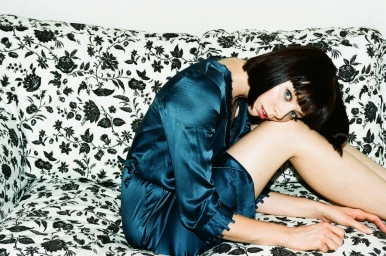 Woman with short dark hair in a teal silk dress seated on a floral patterned sofa