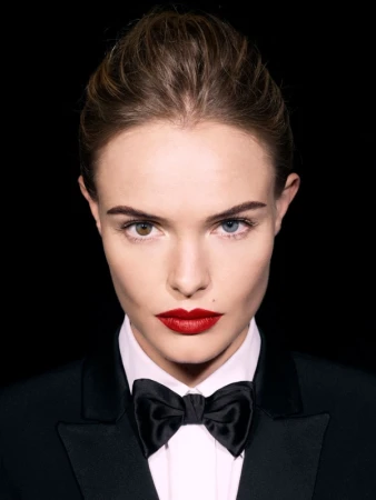 Close-up portrait of a woman in a black tuxedo with a bow tie against a black background with heterochromia and red lipstick.